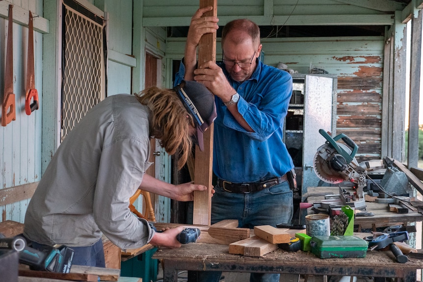 Dom using a drill while his dad holds a piece of timber, north of Longreach, Novemeber 2022.