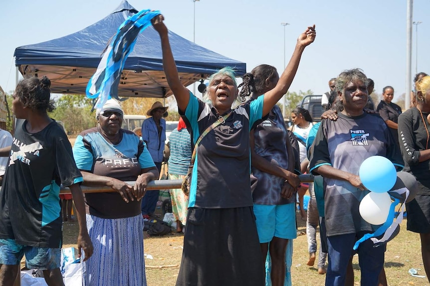 A Power fan raises her hands in the air and waves white, black and teal streamers in a group of supporters.