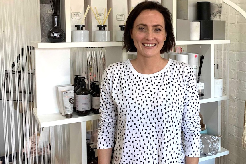 A woman stands in her shop with candles in the background.