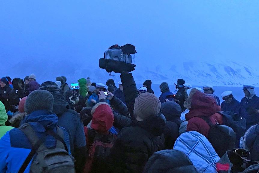 Steven Schubert holding camera above pack of media in gloomy Arctic landscape.