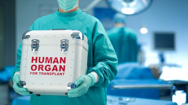 Surgery room with a medical figure in a gown holding a box saying human organ for transplant
