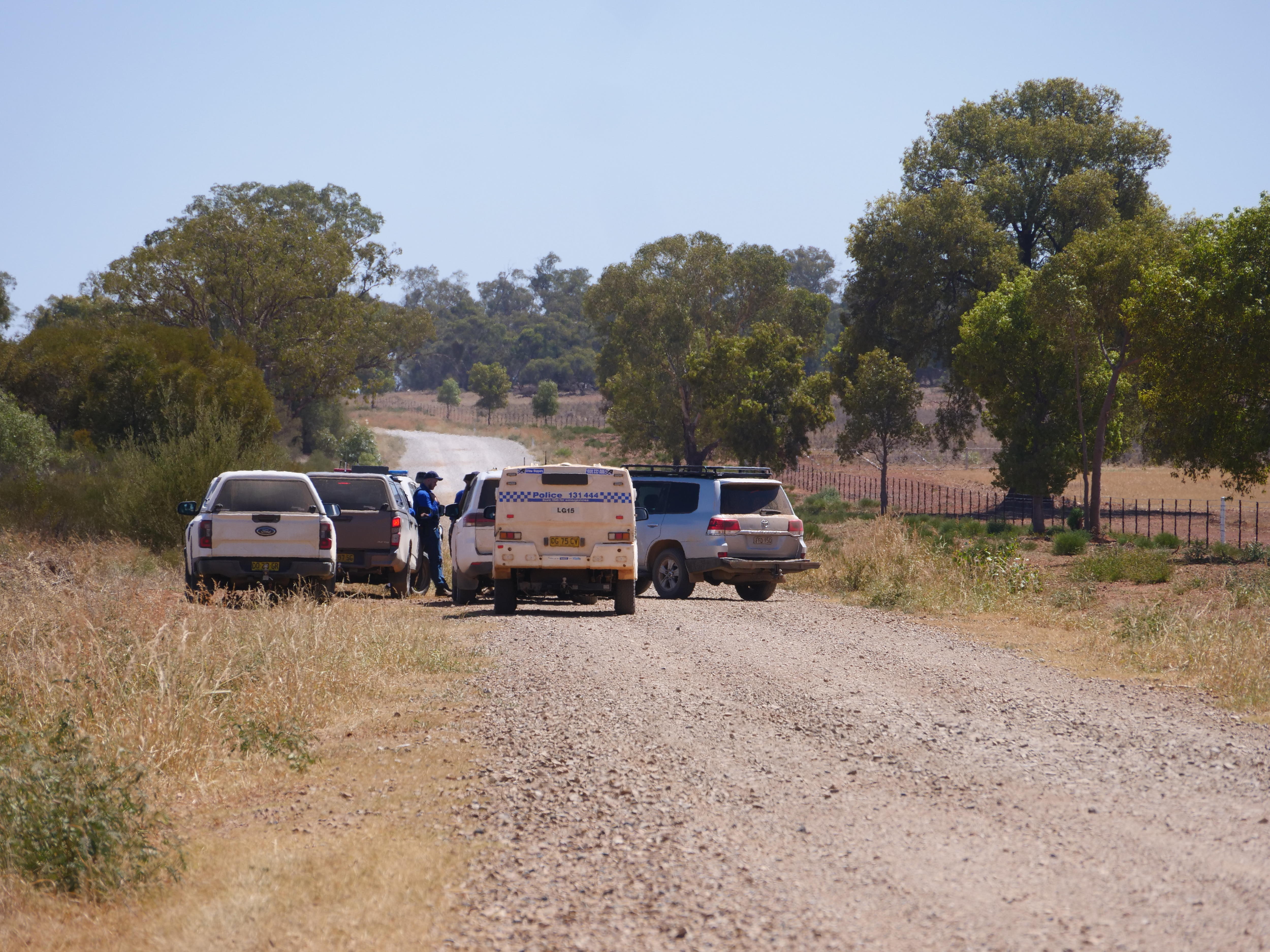 Nova Gales do Sul: Veículos policiais e policiais em uma estrada empoeirada com arbustos e árvores ao fundo.
