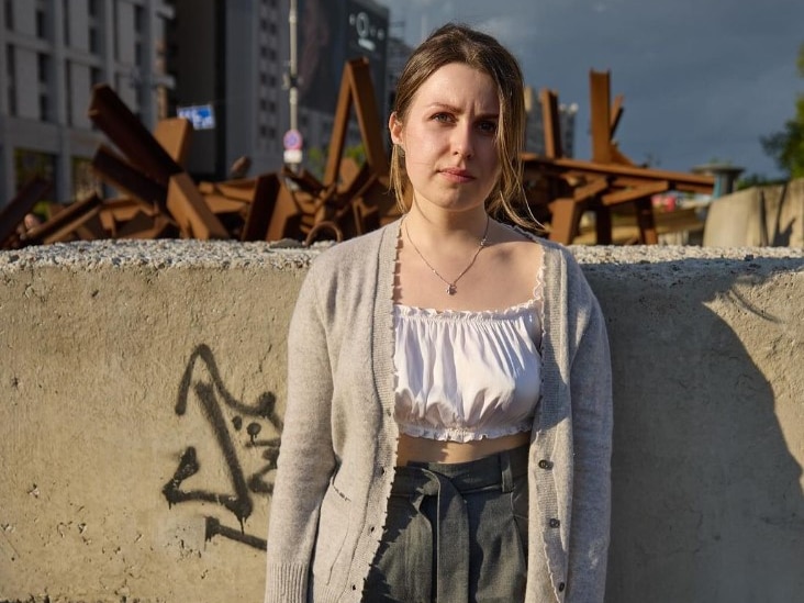 A woman stands in front of a wall in Kyiv. Behind the wall there appears to be a timber baricade