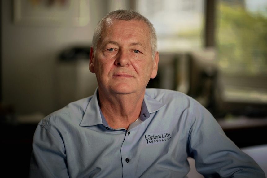 A middle-aged white man with short hair and blue buttoned shirt. He's siting in a chair