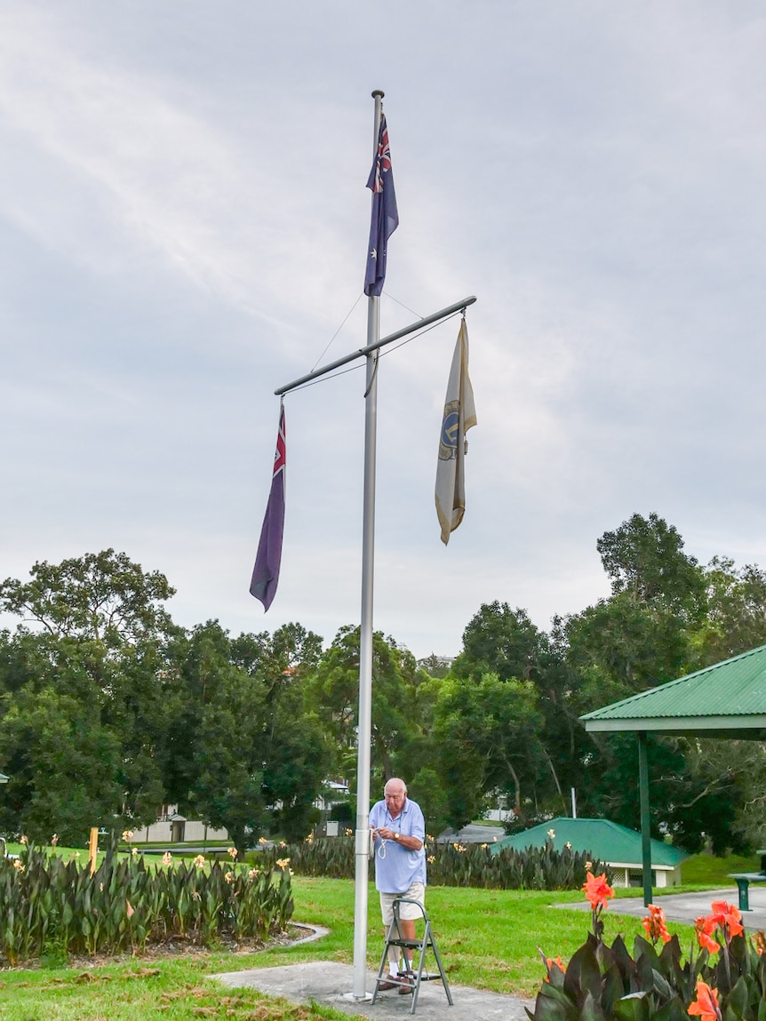 Elderly man hangs a flag up a flagpole.