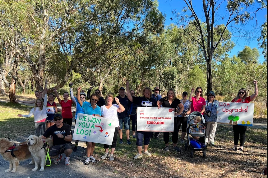 A group of people in sportswear holding up signs and waving hands in a park