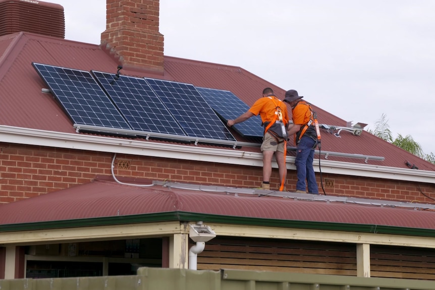 两个人在红砖房和红屋顶的屋顶上安装太阳能电池板