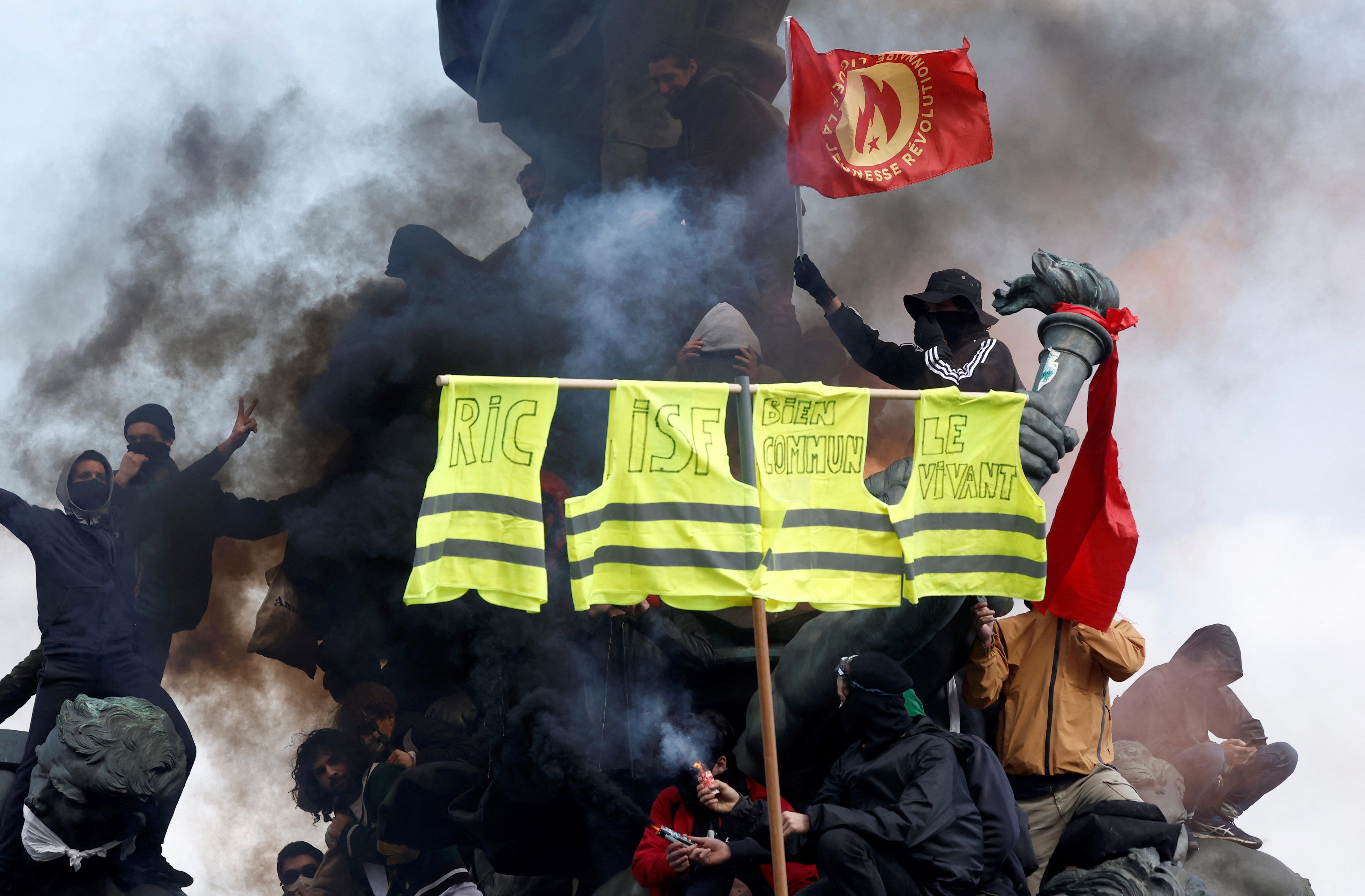 A dozen people climb on and protest with flags, signs and flares as they climb on a statue.