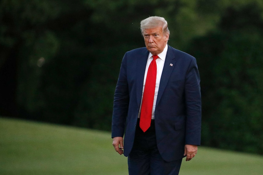 A man in a navy suit and red tie looks ahead as he stands on a lawn.