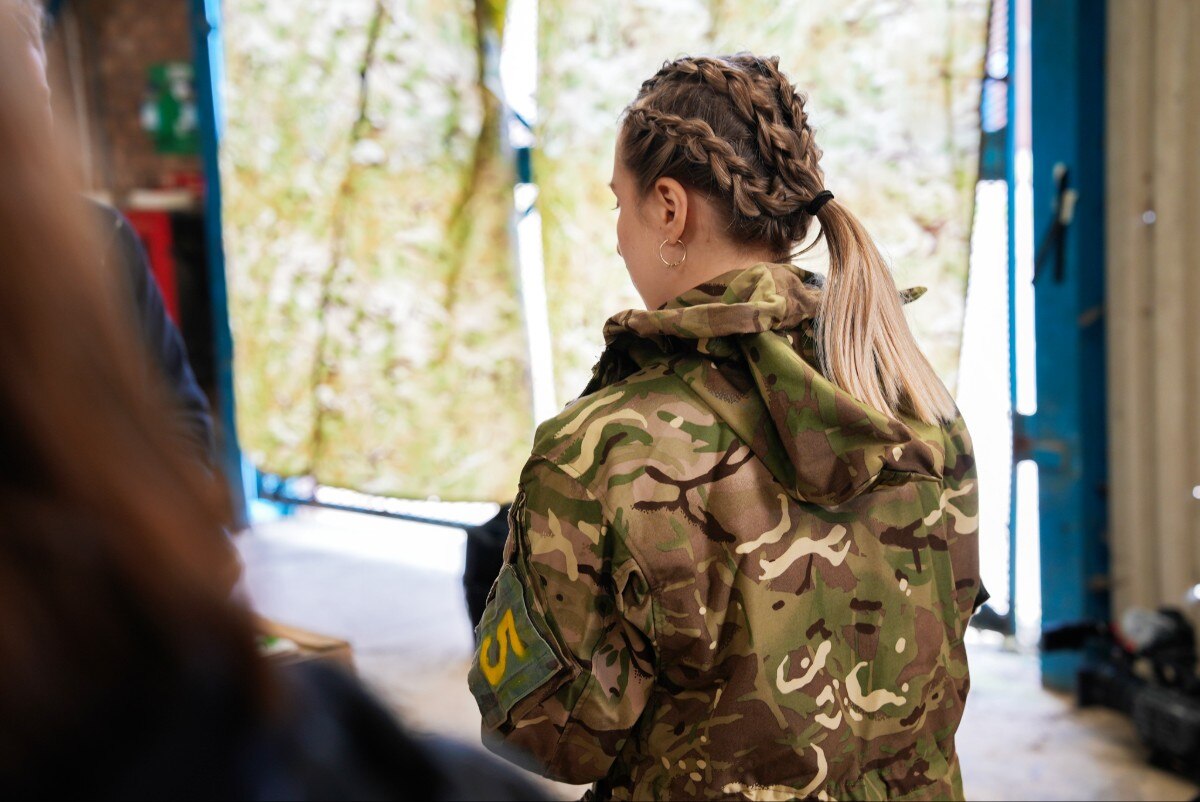 A woman in uniform looking on, with her back to the camera.
