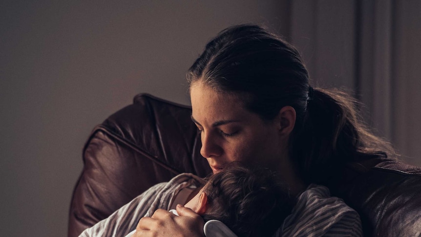 A young mother cradles her baby in her arms, totally absorbed by the moment