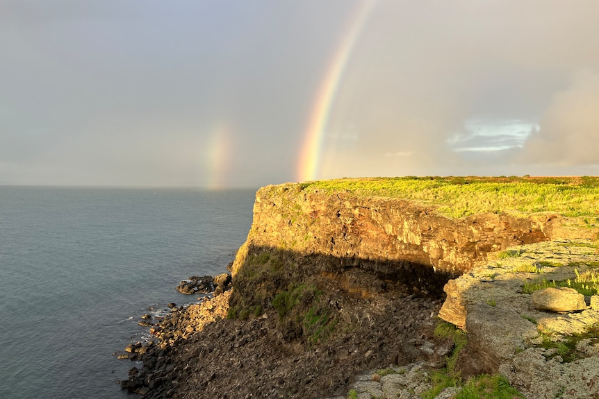 A rainbow is seen off the cliffy coasts of an island.