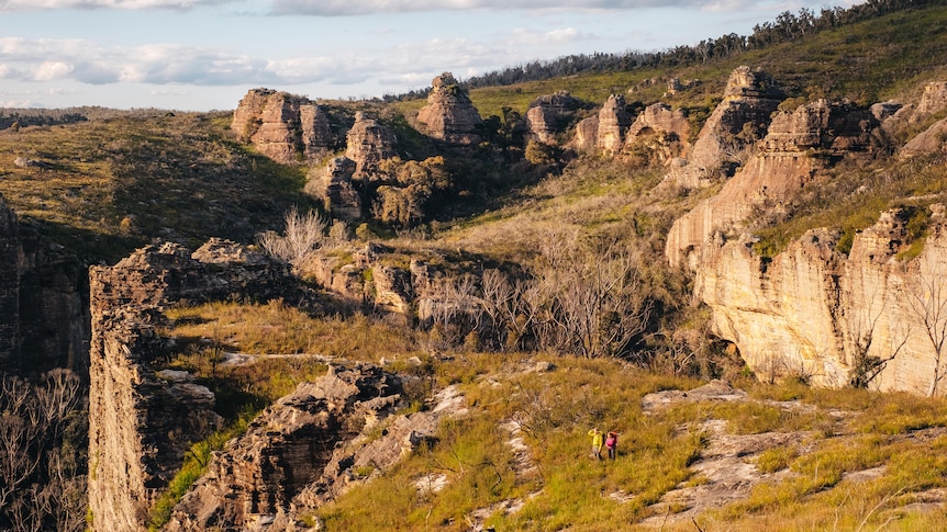 Landscape photo of pagodas and rock formations, with two small hikers on a trail