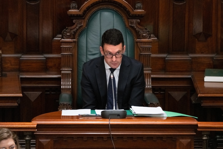 A man in a suit sitting on a wooden throne with a microphone