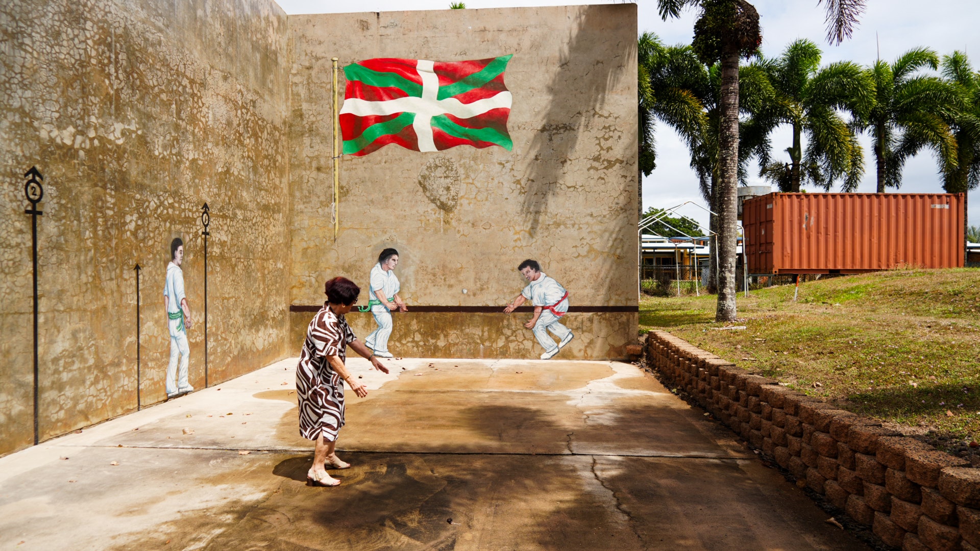 Marie-V Wherry mock hitting a ball against a concrete wall decorated with a Basque mural.