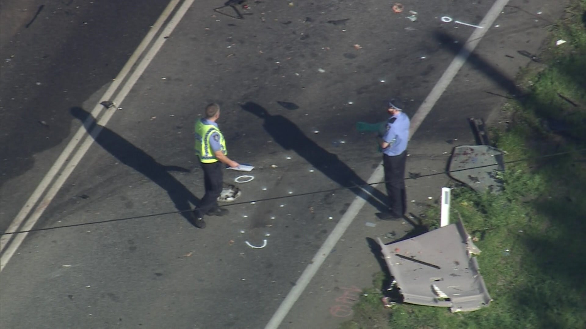 Police stand on the road alongside wreckage from a fatal crash. 