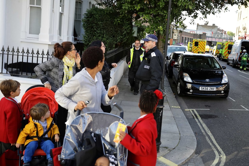 Police officers direct women with children, two of which are in prams, after an explosion in the London Underground.