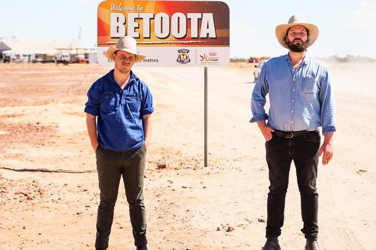 Errol Parker and Clancy Overell stand in front of a Welcome to Betoota sign.