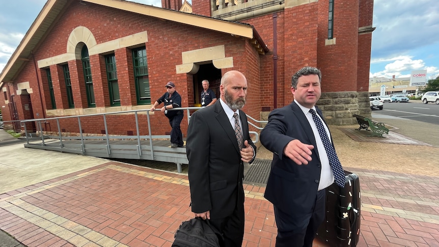 Two men in suits, one with a beard, leave a small court building