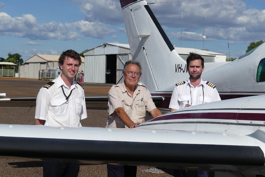 Three men stand alongside a grounded charter plane
