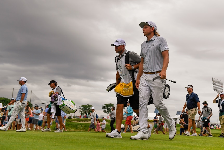 Cameron Smith walks down the fairway next to his caddy with clouds overhead