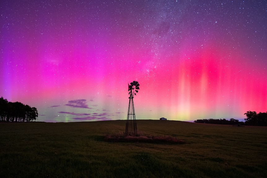 Violet and red lights shimmering in the night sky above a windmill
