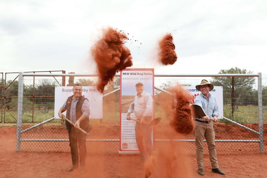 three men flick red dirt up in to the air with shovels.