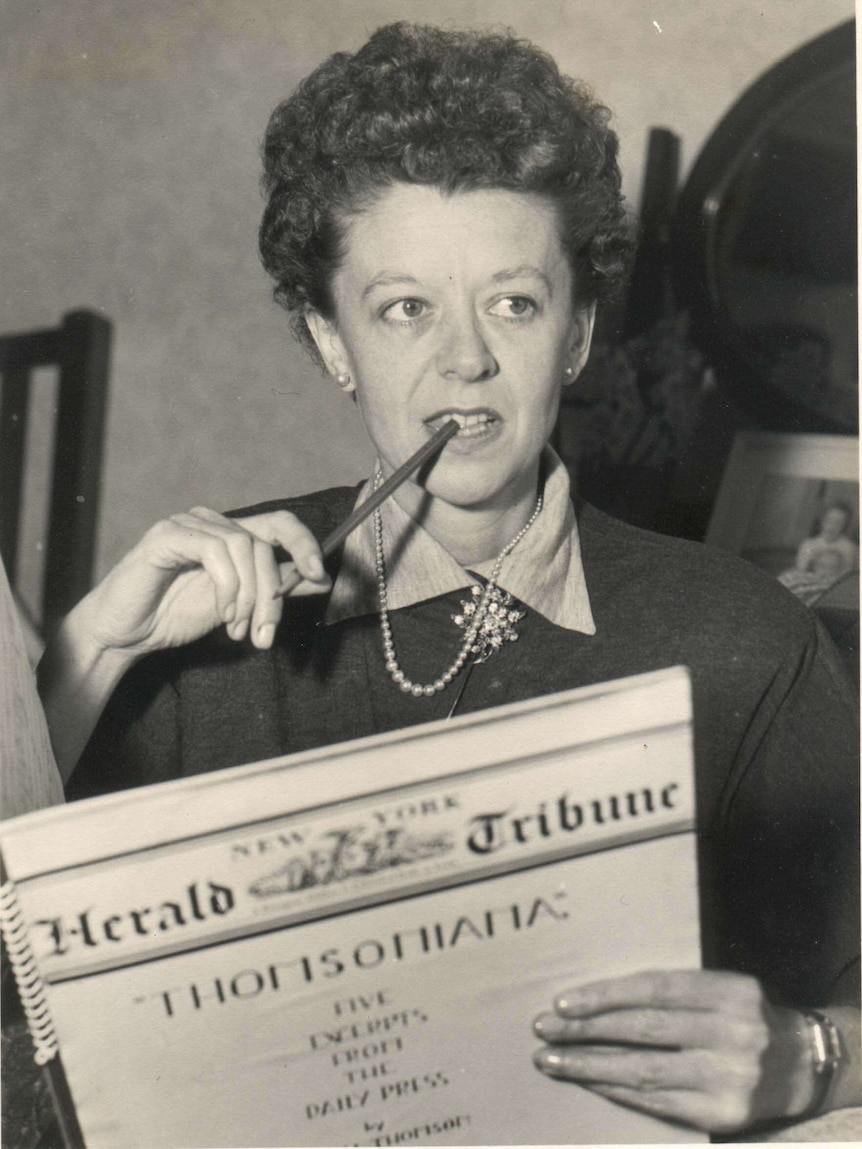 A woman holds a booklet with the New York Herald Tribune's logo on its front, and puts a pencil to her teeth.