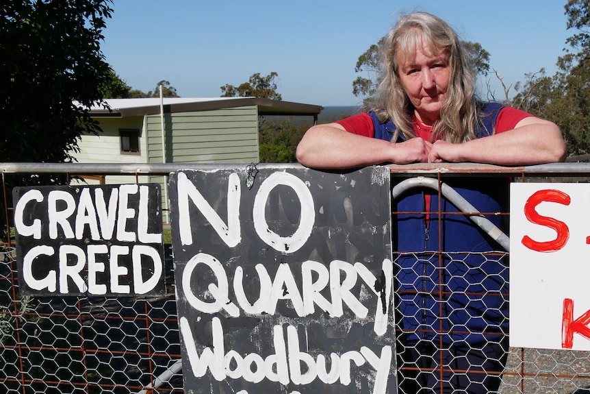 A woman leaning on a fence gate with anti-quarries signs attached to it. 