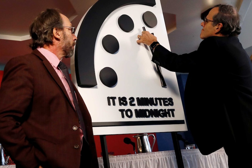 A scientist moves the hands of a model of the Doomsday Clock to two minutes until midnight.