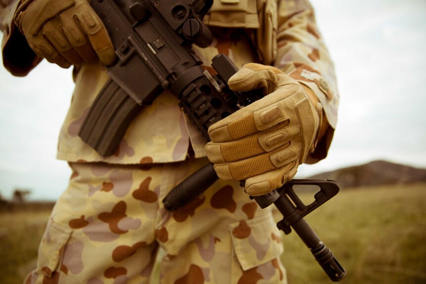 A close up of a weapon being held by a man in army clothing