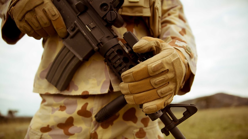 A close up of a weapon being held by a man in army clothing