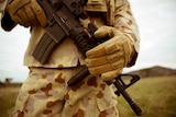 A close up of a weapon being held by a man dressed in special forces army gear.