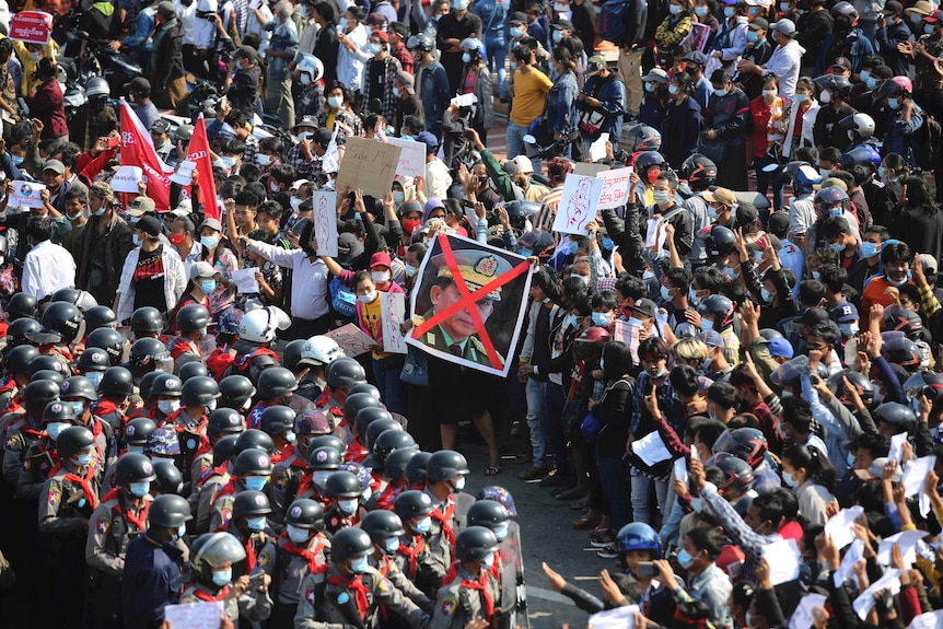 Protesters flashing three fingered salutes and holding an image with an X on the face of a general face off with police