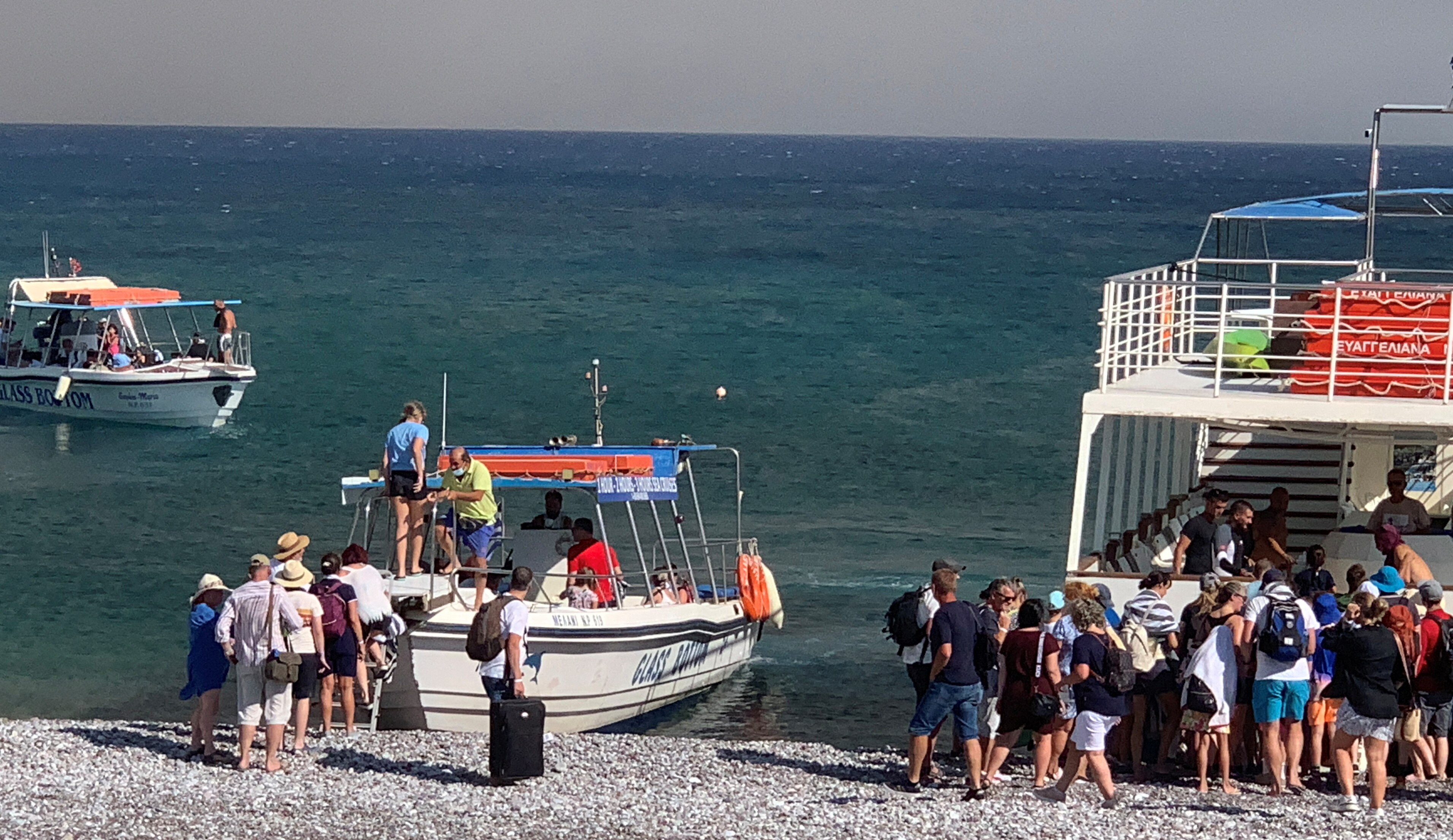 Tourists board two boats which have anchored on the shore of a beach on the island of Rhodes
