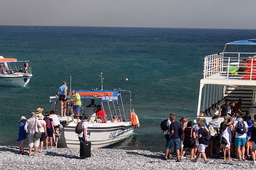 Tourists board two boats which have anchored on the shore of a beach on the island of Rhodes