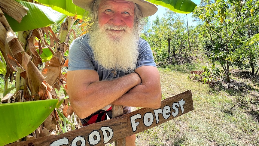 A bearded man in a hat leaning over a sign in front of trees