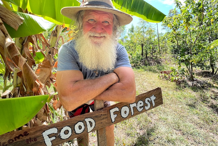 A bearded man in a hat leaning over a sign in front of trees