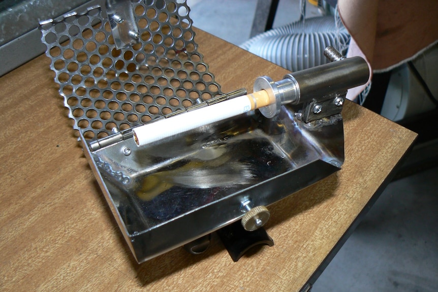 A metal contraption holds a cigarette and it has a cage around it, with a metal tube for sucking on.