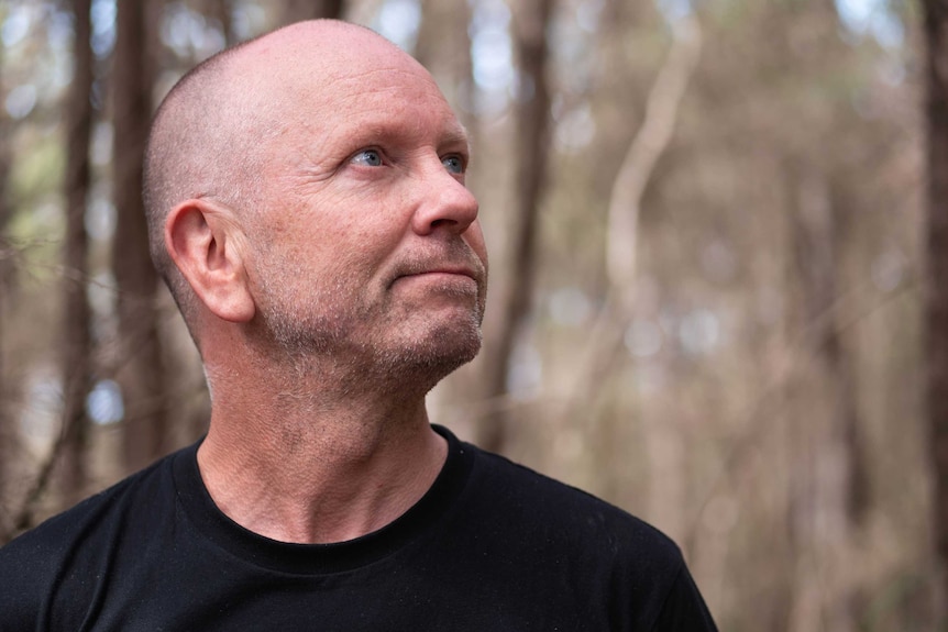 A head shot of Heath Garratt looking into the distance with blurred out forest behind him.