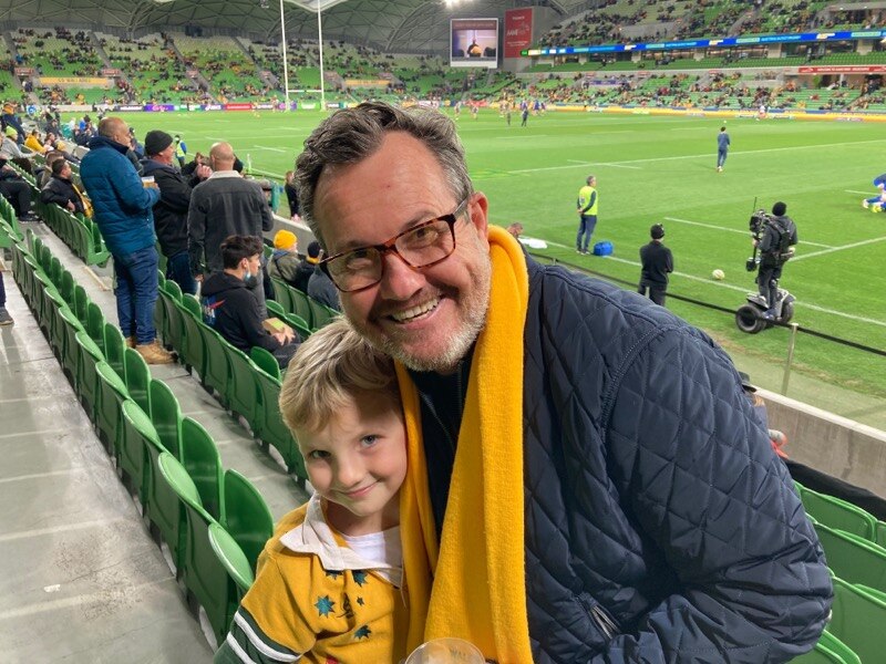A man and a young girl in an Australia rugby top waiting for a game of rugby to start at a stadium