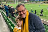 A man and a young girl in an Australia rugby top waiting for a game of rugby to start at a stadium