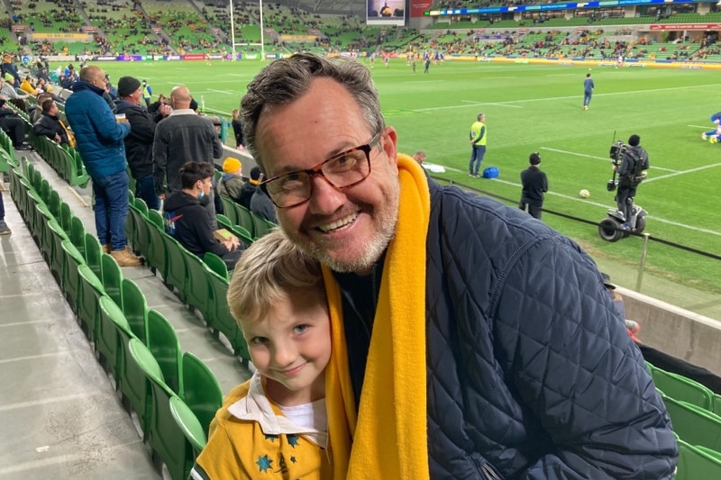 A man and a young girl in an Australia rugby top waiting for a game of rugby to start at a stadium