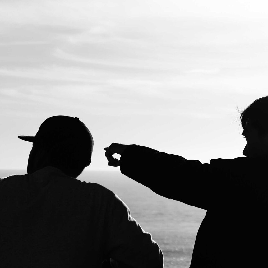 Two men standing in silhouette at the beach.