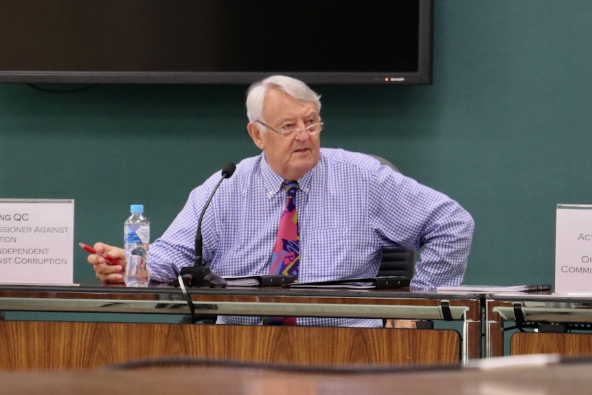 NT Anti-corruption commissioner Ken Fleming sits at a desk in NT Parliament, looking concerned.