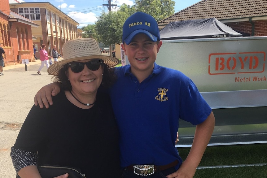 Smiling woman in black wearing a hat standing next to a smiling boy in a blue shirt, jeans and a cap