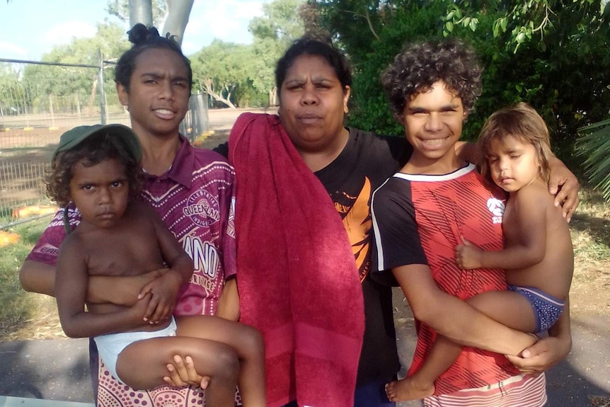 An Aboriginal family stands together with trees behind them