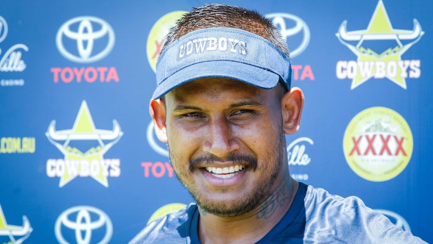 Ben Barba, wearing a North Queensland Cowboys visor, stands in front of an advertising while speaking to the media.