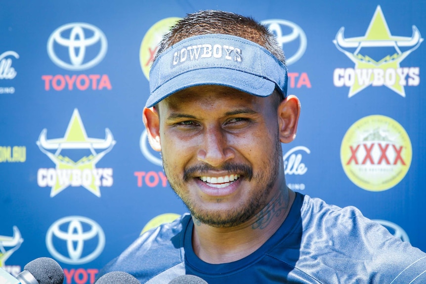 Ben Barba, wearing a North Queensland Cowboys visor, stands in front of an advertising while speaking to the media.