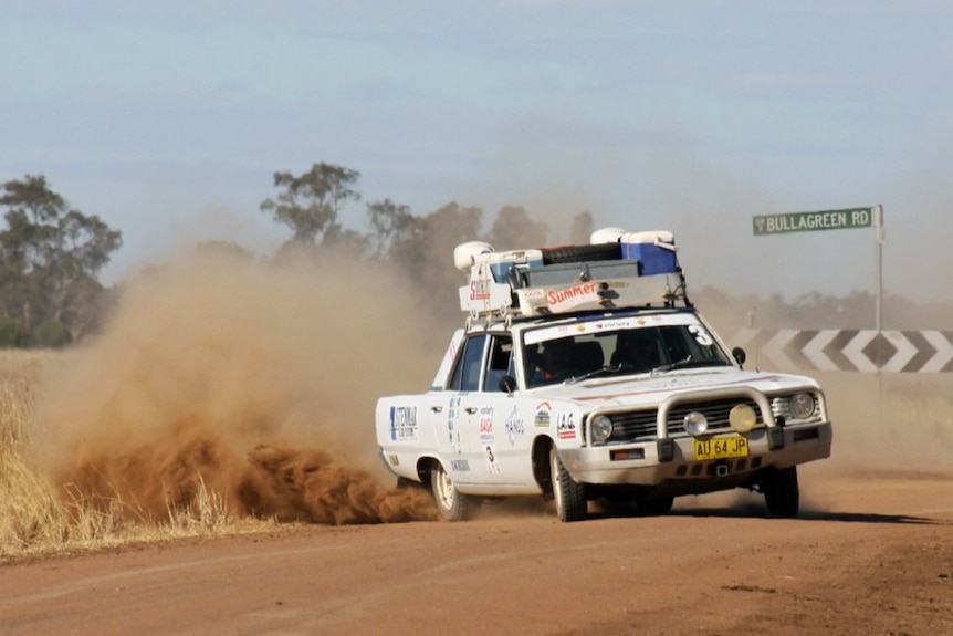 A white car raises a cloud of dust on a dirt road.
